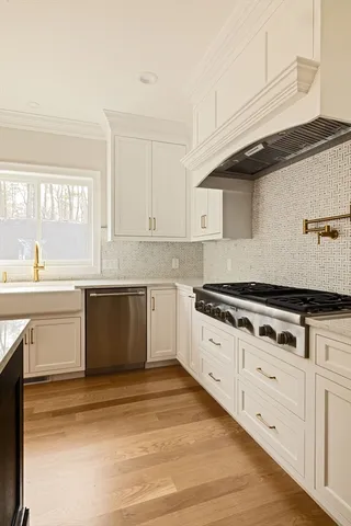 a large white kitchen with granite countertop a stove a sink dishwasher and white cabinets with wooden floor