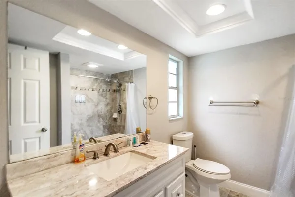 a bathroom with a granite countertop sink a toilet a mirror and a shower