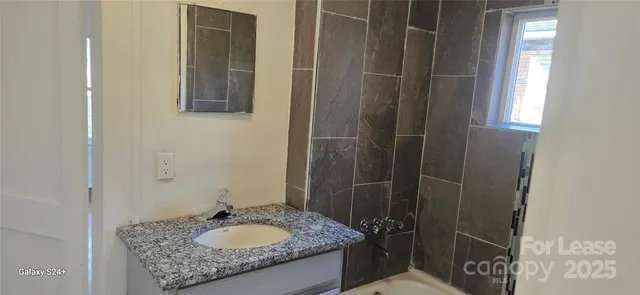 a bathroom with a granite countertop sink a mirror and shower