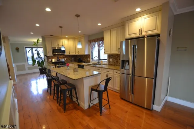 a kitchen with stainless steel appliances granite countertop a refrigerator a stove a sink a dining table and chairs with wooden floor