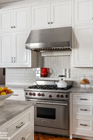 a kitchen with stainless steel appliances granite countertop a sink a stove a chimney a refrigerator and chairs