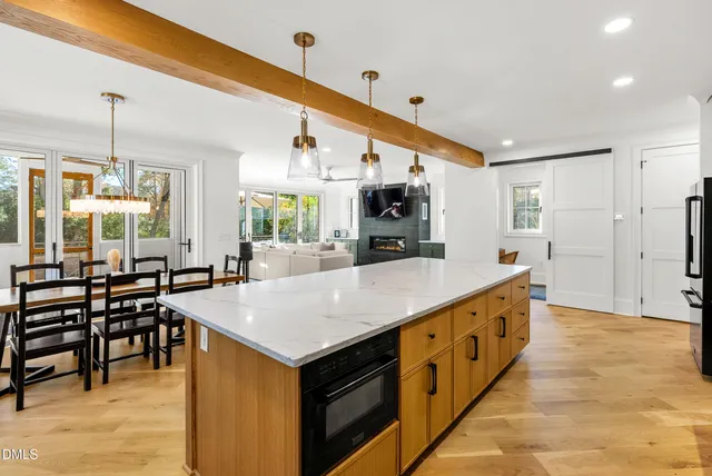 a kitchen with stainless steel appliances kitchen island granite countertop a refrigerator a stove a sink a dining table and chairs with wooden floor