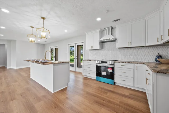 a large kitchen with granite countertop a stove a sink a center island and wooden floor