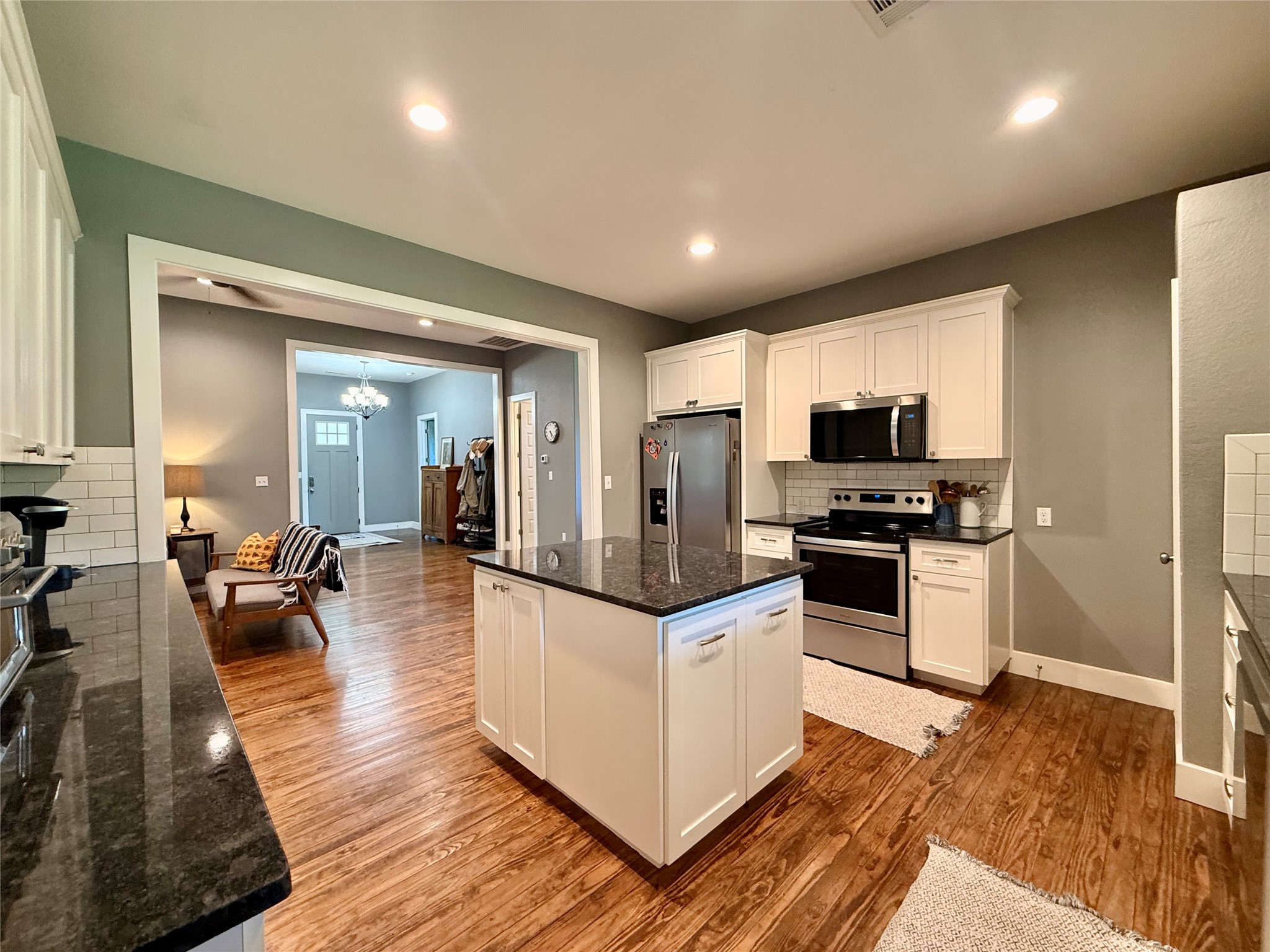 739 Pleasant Grove Road Elgin, TX 78621 - Photo 9 of 29 Kitchen featuring a central island with dark countertop, white cabinetry, stainless steel appliances, and wood-finish flooring