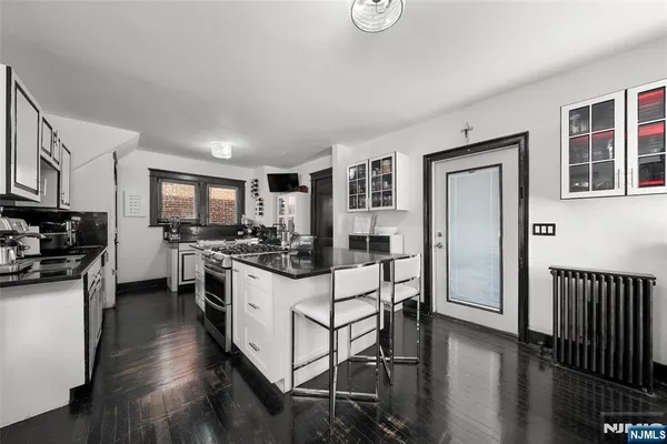 a kitchen with stainless steel appliances kitchen island granite countertop a stove top oven a sink a refrigerator white cabinets and wooden floor