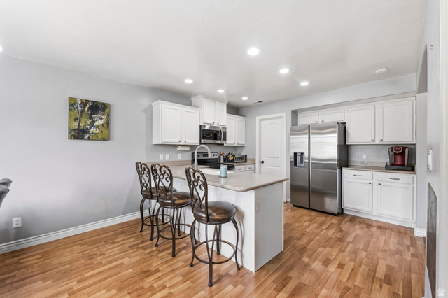 1165 West 100 South Springville, UT 84663 - Photo 7 of 28 Kitchen featuring stainless steel appliances, white cabinetry, light countertops, a breakfast bar area, and light wood-style flooring