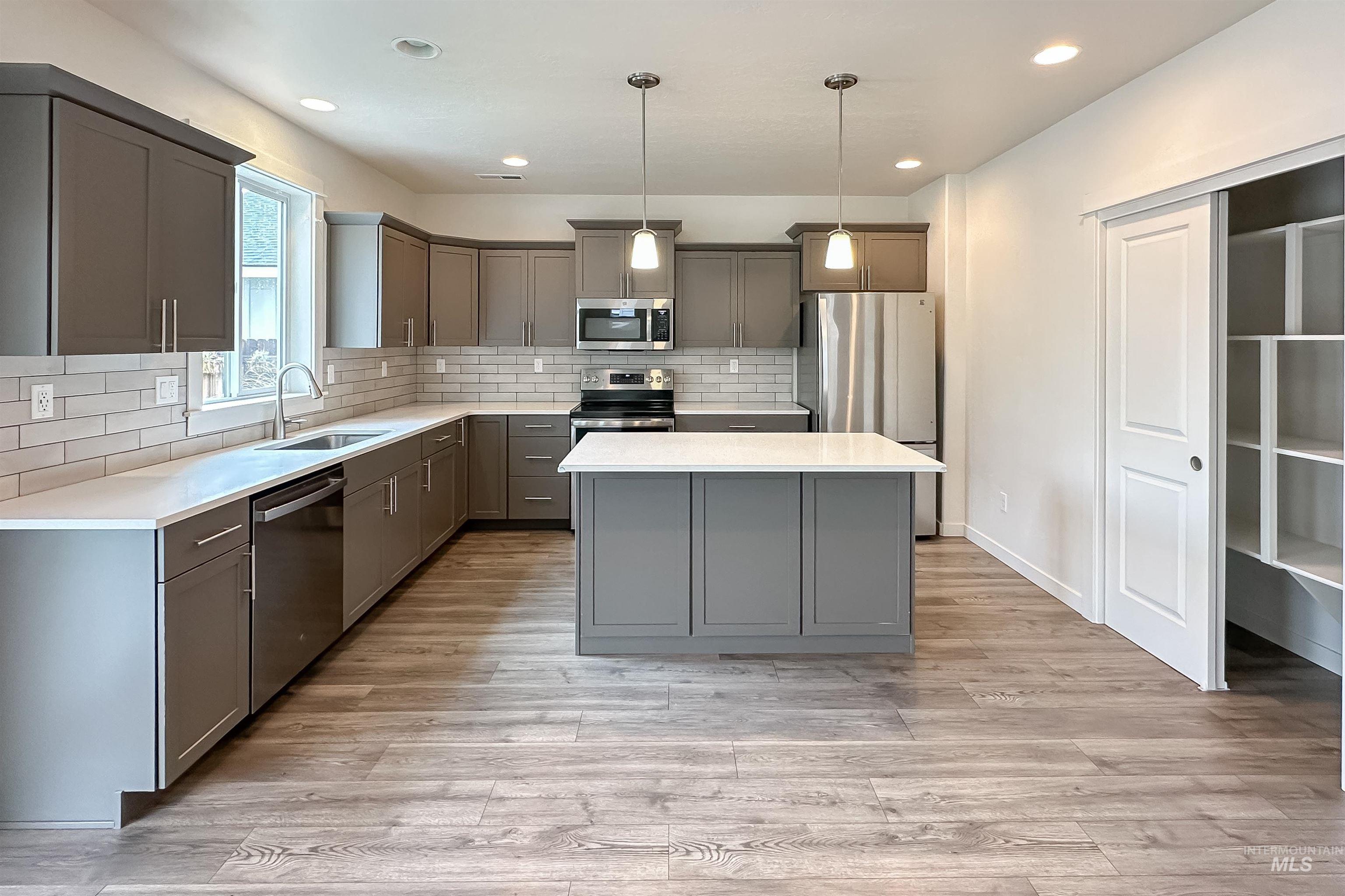 9687 West Arnold Road Boise, ID 83714 - Photo 9 of 37 Modern kitchen featuring wood-finish flooring, grey cabinetry, white countertops, a tiled backsplash, and a central island with pendant lighting
