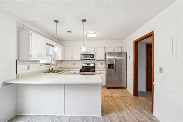 a kitchen with stainless steel appliances granite countertop a refrigerator a sink a stove and white cabinets with wooden floor