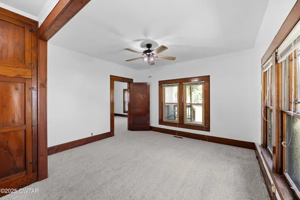an empty room with chandelier fan and windows