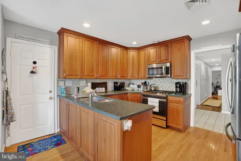 a kitchen with stainless steel appliances granite countertop a refrigerator a sink dishwasher a stove and white countertops with wooden floor