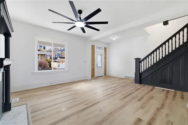 a view of an empty room with wooden floor and a ceiling fan
