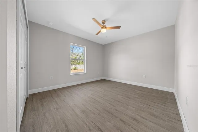 an empty room with wooden floor ceiling fan and windows