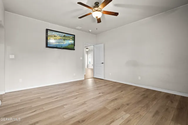 a view of an empty room with wooden floor and a ceiling fan