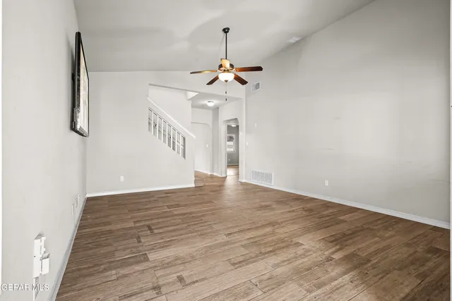 a view of an empty room with chandelier fan and wooden floor