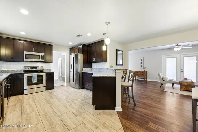 a kitchen with stainless steel appliances kitchen island granite countertop a refrigerator a stove top oven a sink dishwasher and white cabinets with wooden floor