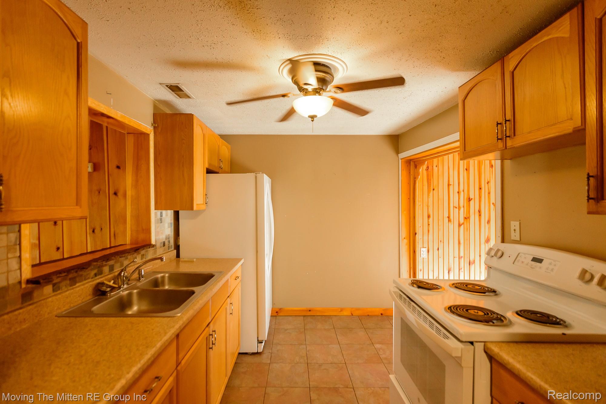 26247 Weigel Road New Boston, MI 48164 - Photo 10 of 30 Wood cabinetry with dark hardware, dual basin stainless steel sink, patterned tile backsplash, white electric range, and ceiling fan with integrated lighting