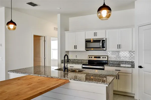 a kitchen with stainless steel appliances granite countertop a sink a microwave a refrigerator and white cabinets