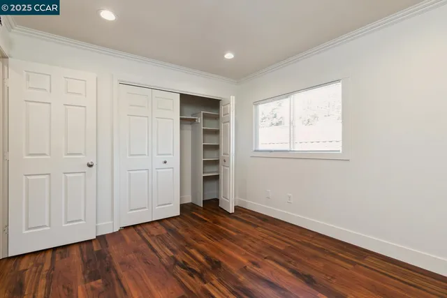 an empty room with wooden floor closet and windows