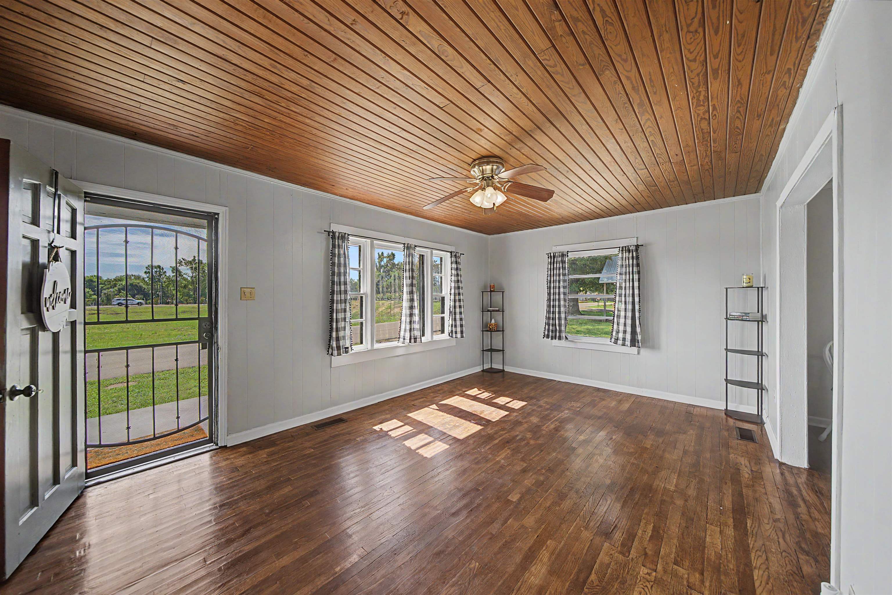201 Walnut Street Adamsville, TN 38310 - Photo 15 of 26 Living area featuring wood-finish flooring, a planked wood ceiling, a ceiling fan with integrated lighting, multiple windows, and a front entry door with a security screen