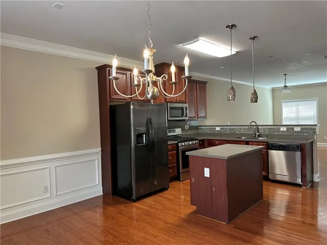 an empty room with wooden floor and kitchen view