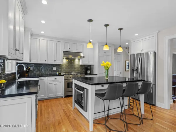 a kitchen with stainless steel appliances granite countertop a stove top oven a refrigerator a sink and white cabinets with wooden floor