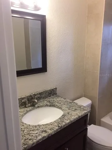 a bathroom with a granite countertop toilet sink and mirror