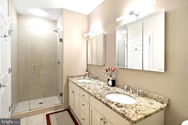 a bathroom with a granite countertop double vanity sink mirror and shower