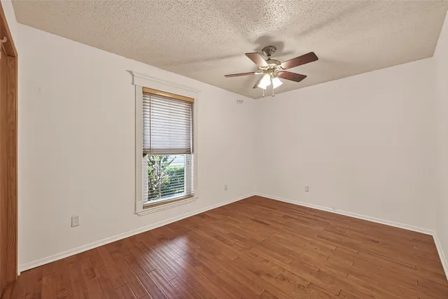 an empty room with wooden floor ceiling fan and windows