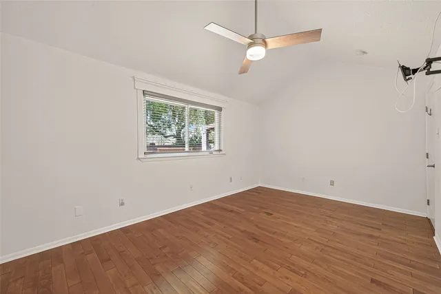 an empty room with wooden floor ceiling fan and window