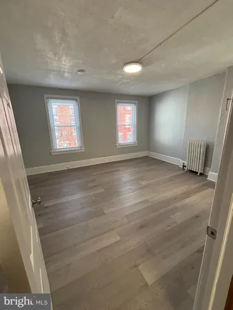 a view of an empty room with wooden floor and kitchen view