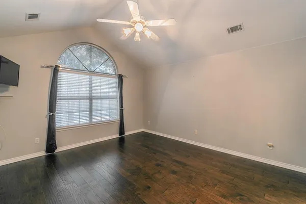 an empty room with wooden floor chandelier fan and windows