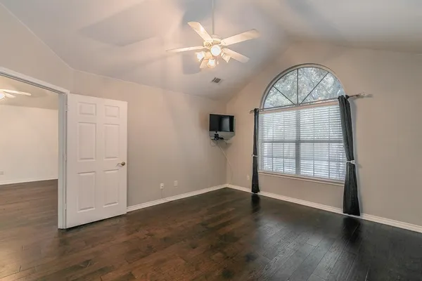 an empty room with wooden floor chandelier fan and windows
