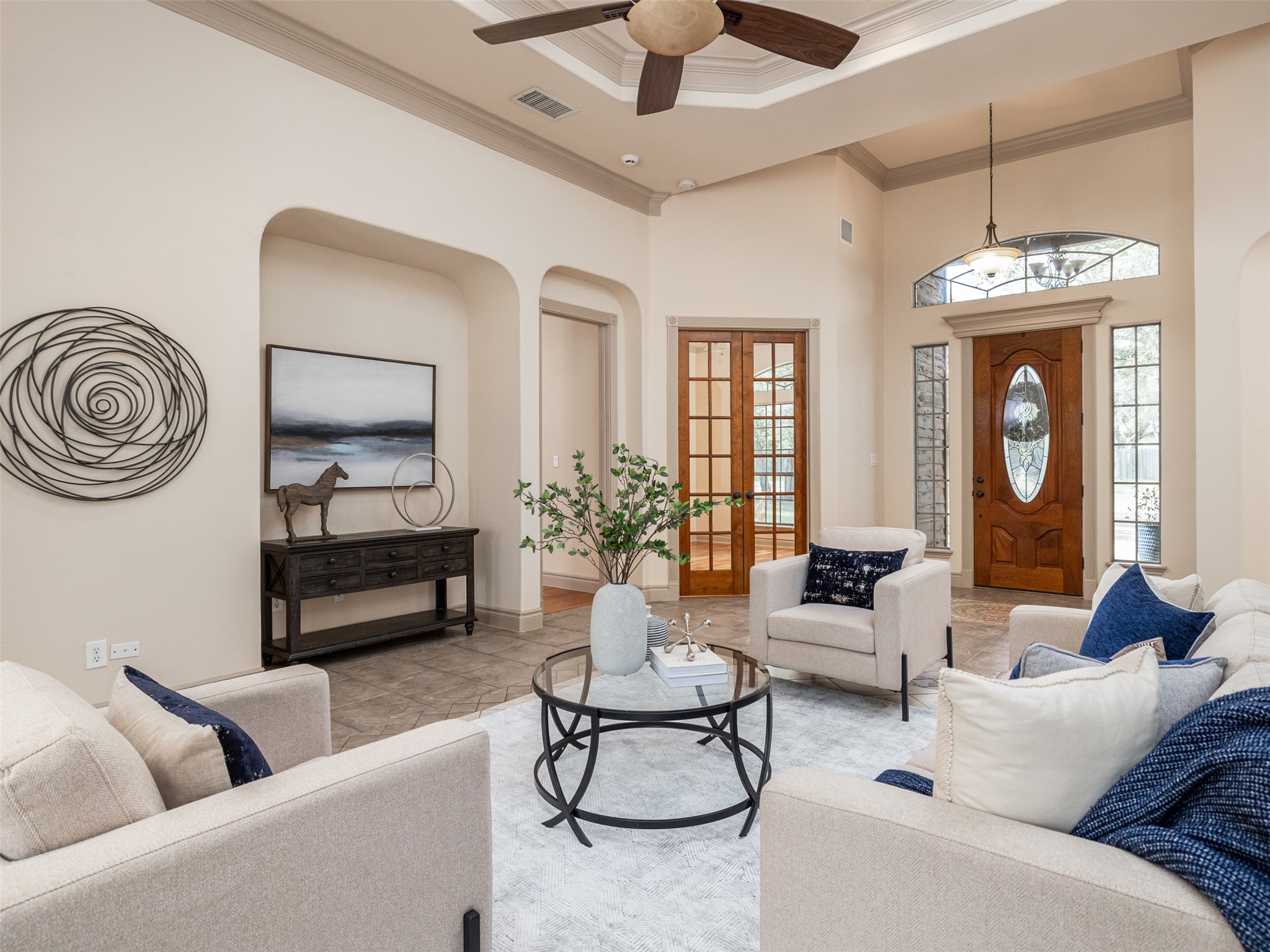 Living room with a high ceiling, arched walkways, ceiling fan, crown molding, and tile patterned flooring