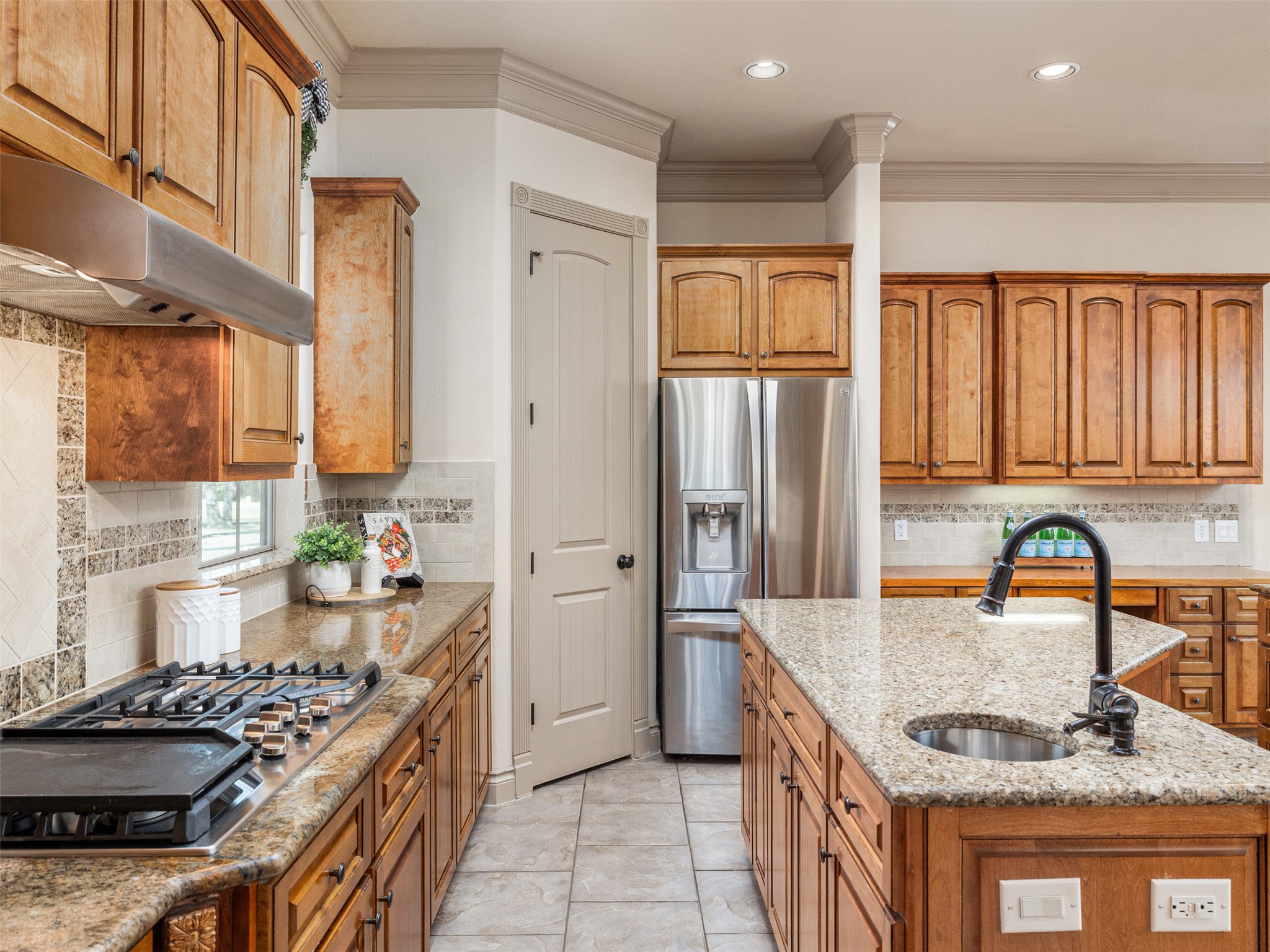 139 Ware Drive Buda, TX 78610 - Photo 9 of 39 Kitchen with stainless steel appliances, wood finish cabinetry, an island with sink, light stone countertops, and crown molding