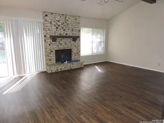 an empty room with wooden floor fireplace and windows