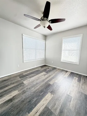 an empty room with wooden floor ceiling fan and windows