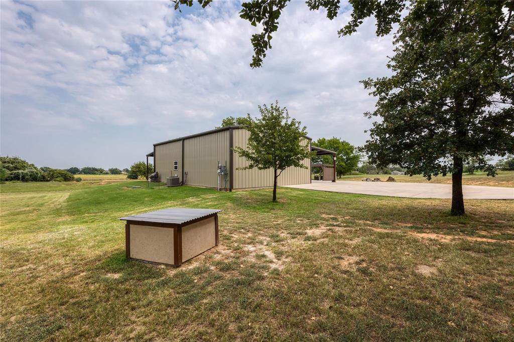 210 Spring Branch Trail North Springtown, TX 76082 - Photo 27 of 36 Metal construction building with an attached covered entry, extensive concrete hardscaping, and mature trees