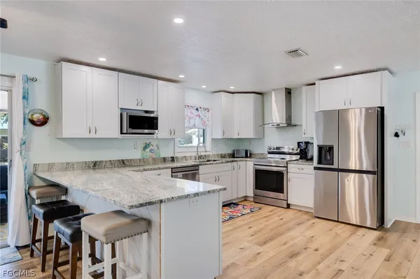 a kitchen with granite countertop a stove top oven a sink dishwasher a refrigerator and white cabinets with wooden floor