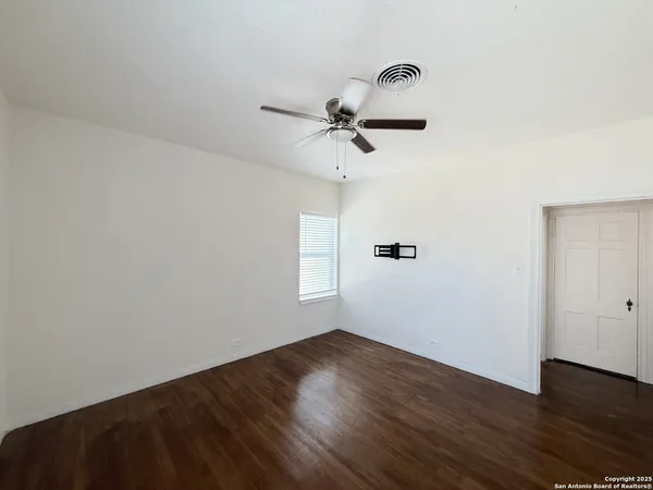 an empty room with wooden floor ceiling fan and window