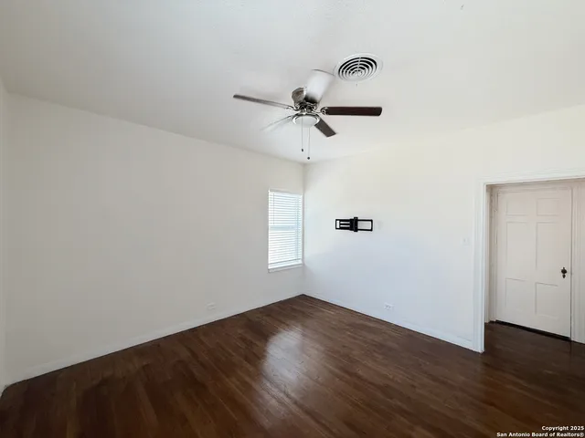an empty room with wooden floor ceiling fan and window