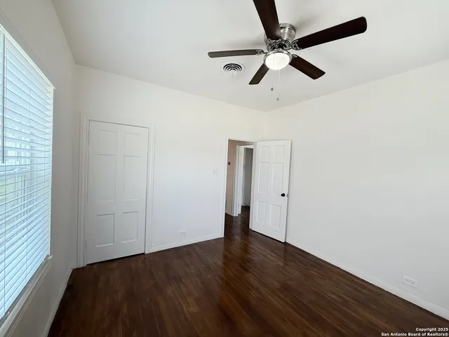 an empty room with wooden floor ceiling fan and windows