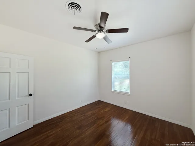 an empty room with wooden floor fan and windows