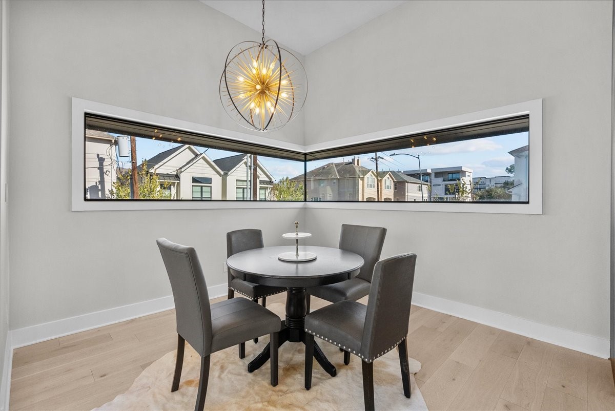 516 Reinerman Street Houston, TX 77007 - Photo 18 of 42 This photo showcases a modern dining nook with a round table and four chairs. The space features large corner windows with a view of neighboring houses, light wood flooring, and a stylish pendant light, creating a bright and inviting atmosphere.
