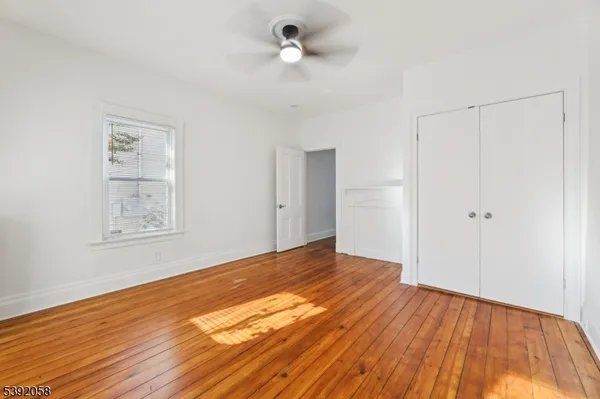 a view of an empty room with wooden floor and a ceiling fan