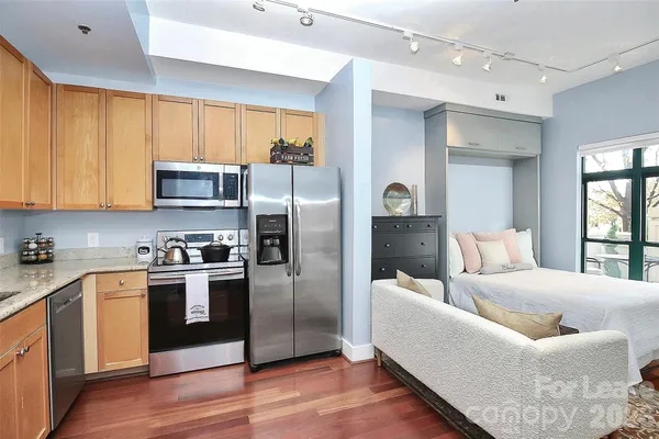 a large kitchen with stainless steel appliances granite countertop a refrigerator a stove top oven a sink and dishwasher with wooden floor