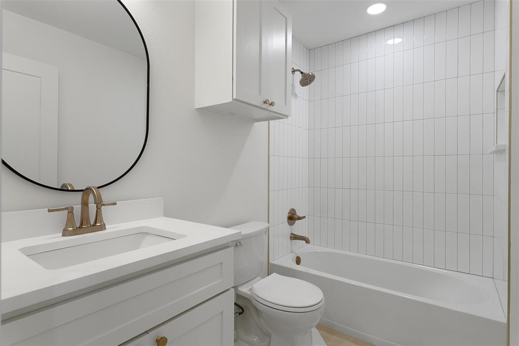 1346 South Reno Road Springtown, TX 76082 - Photo 14 of 24 Bathroom featuring a white vanity with an integrated sink, brushed gold fixtures, a contemporary oval mirror, a white toilet, and a tiled shower-over-tub with a recessed niche
