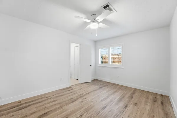an empty room with wooden floor fan and windows