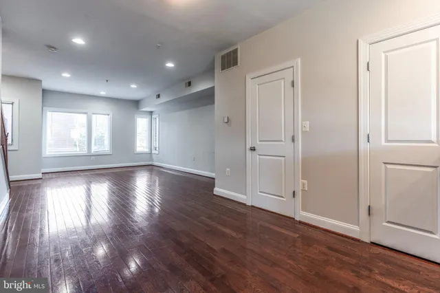 an empty room with wooden floor and windows with curtains