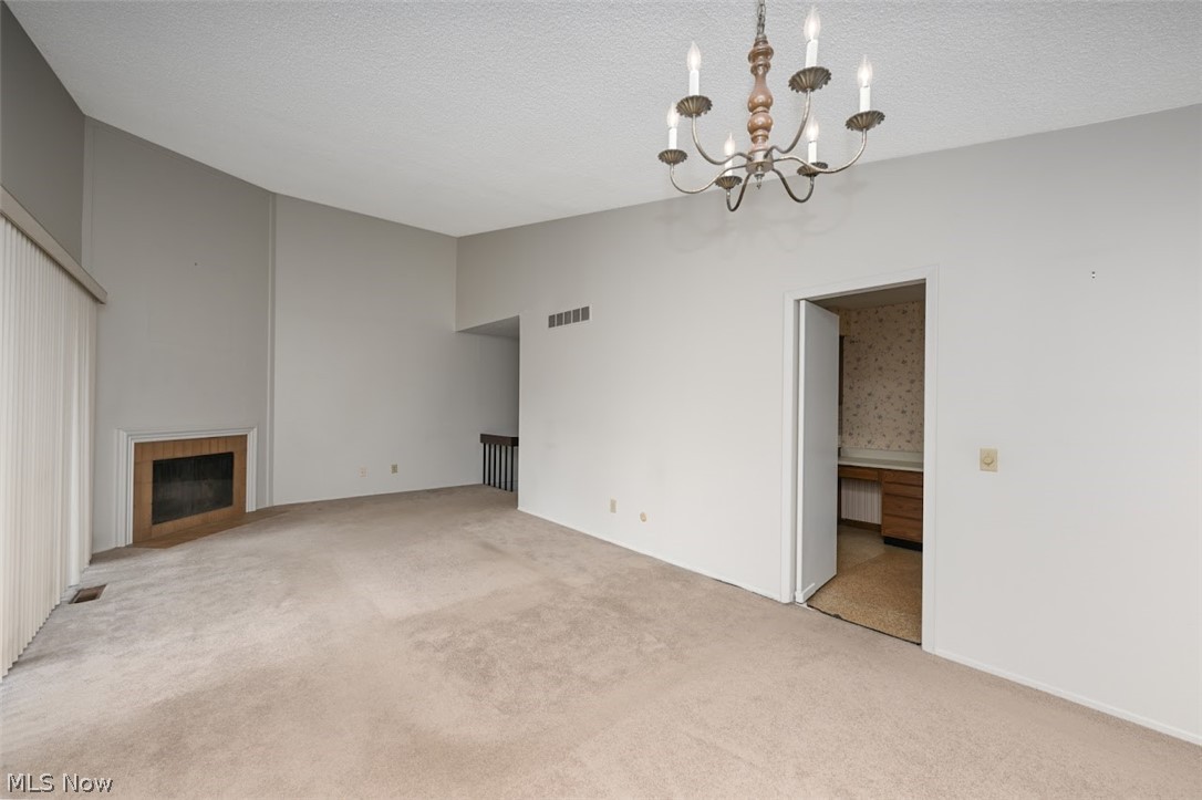 979 Hampton Ridge Drive Akron, OH 44313 - Photo 9 of 25 Unfurnished living room featuring a textured ceiling, a fireplace, a high ceiling, a chandelier, and light colored carpet