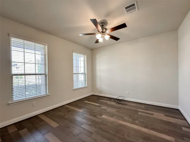 an empty room with wooden floor fan and windows